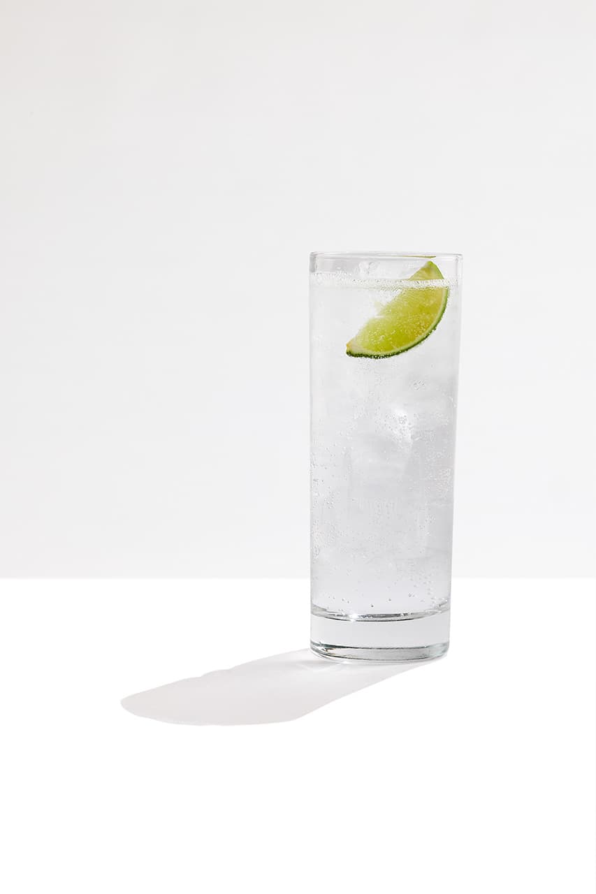 A Gin & Tonic cocktail made with Tanqueray London Dry Gin garnished with two lime slices. A bottle of Tanqueray London Dry gin sits in the background of the image.