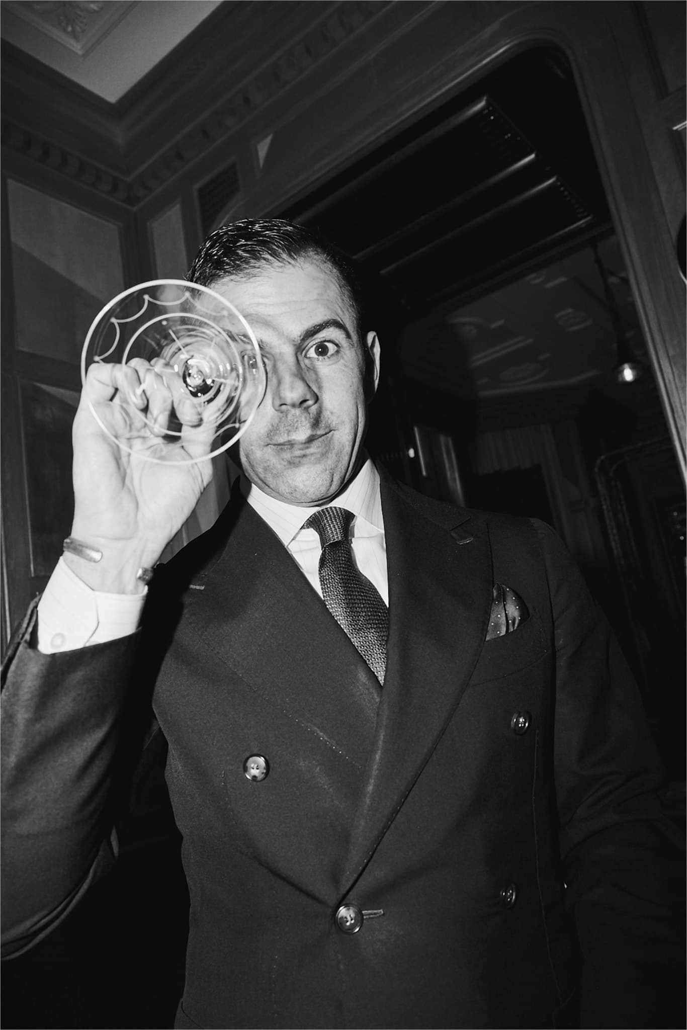 Ago Perrone with a martini glass up to his right eye.