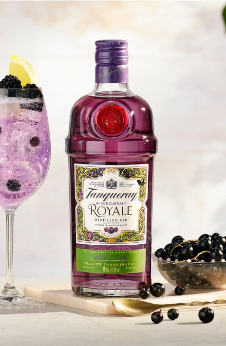 A bottle of Royal on a table next to a cocktail and blackcurrants.