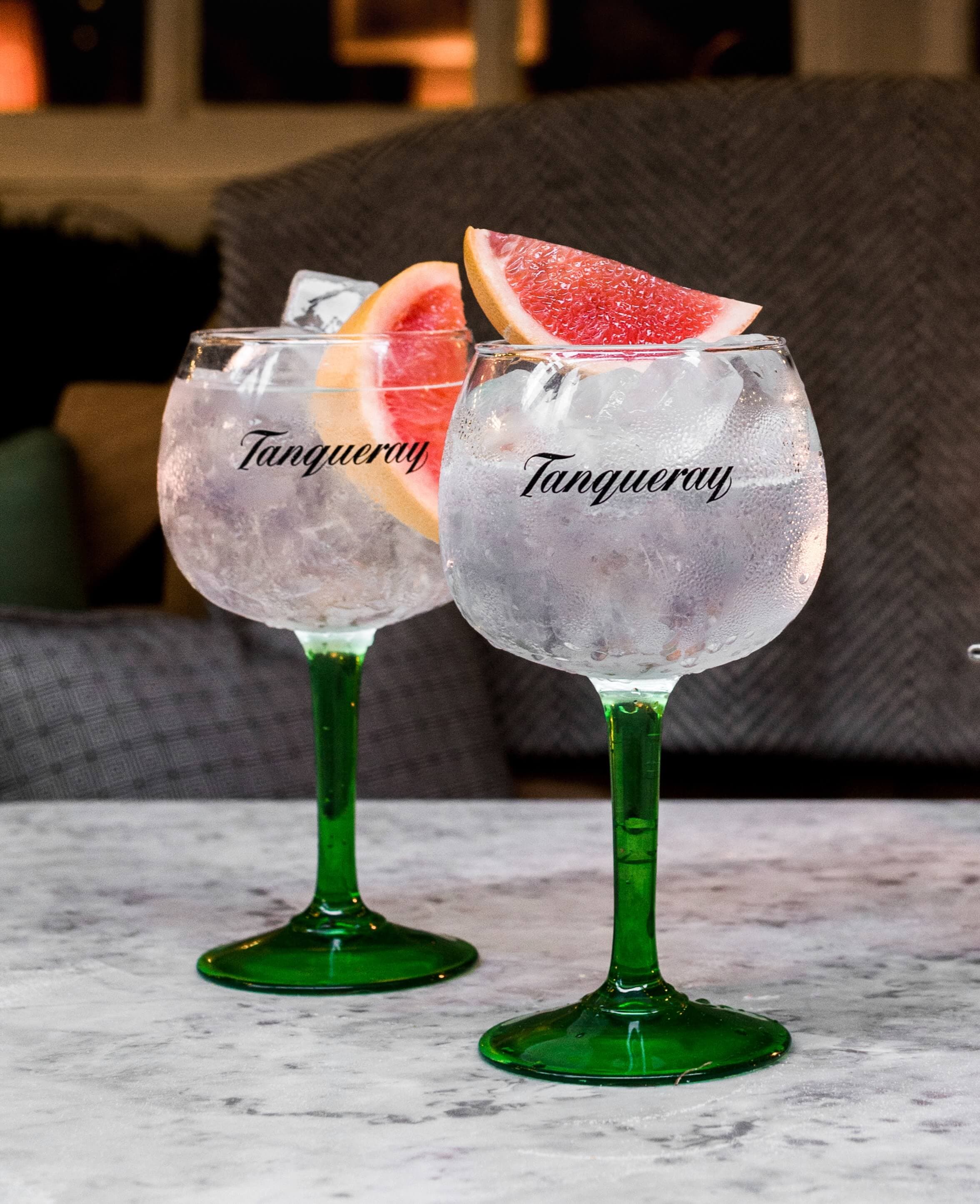 Two Gin & Tonic cocktails made with Tanqueray No. Ten, garnished with grapefruit slices. Both cocktails are in Tanqueray branded glasses.